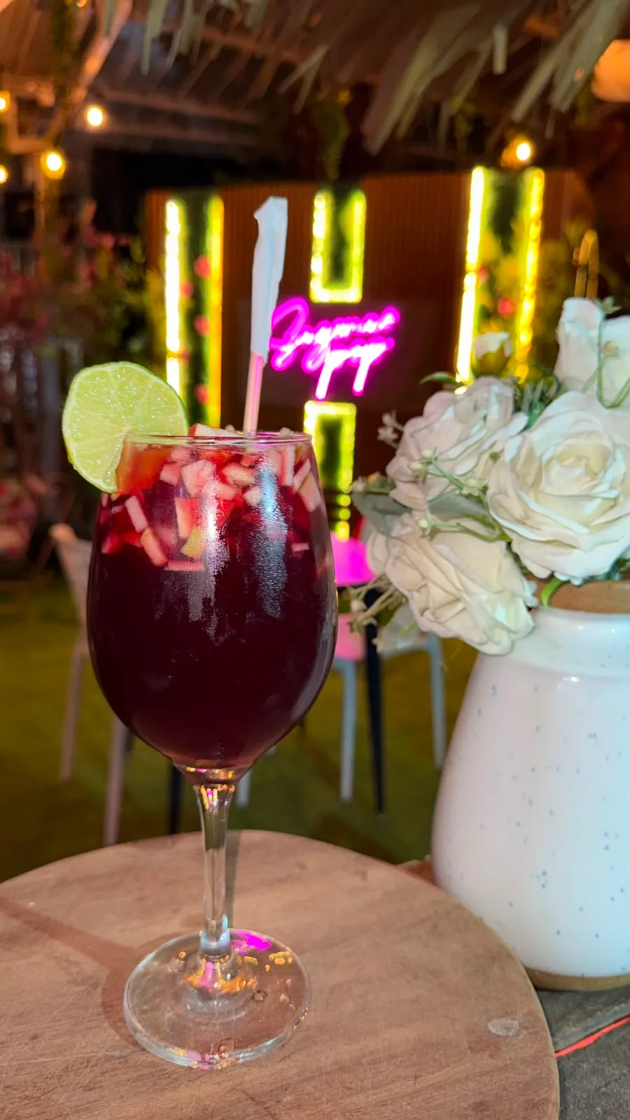 Copa de sangría con frutas junto a un ramo de rosas blancas.