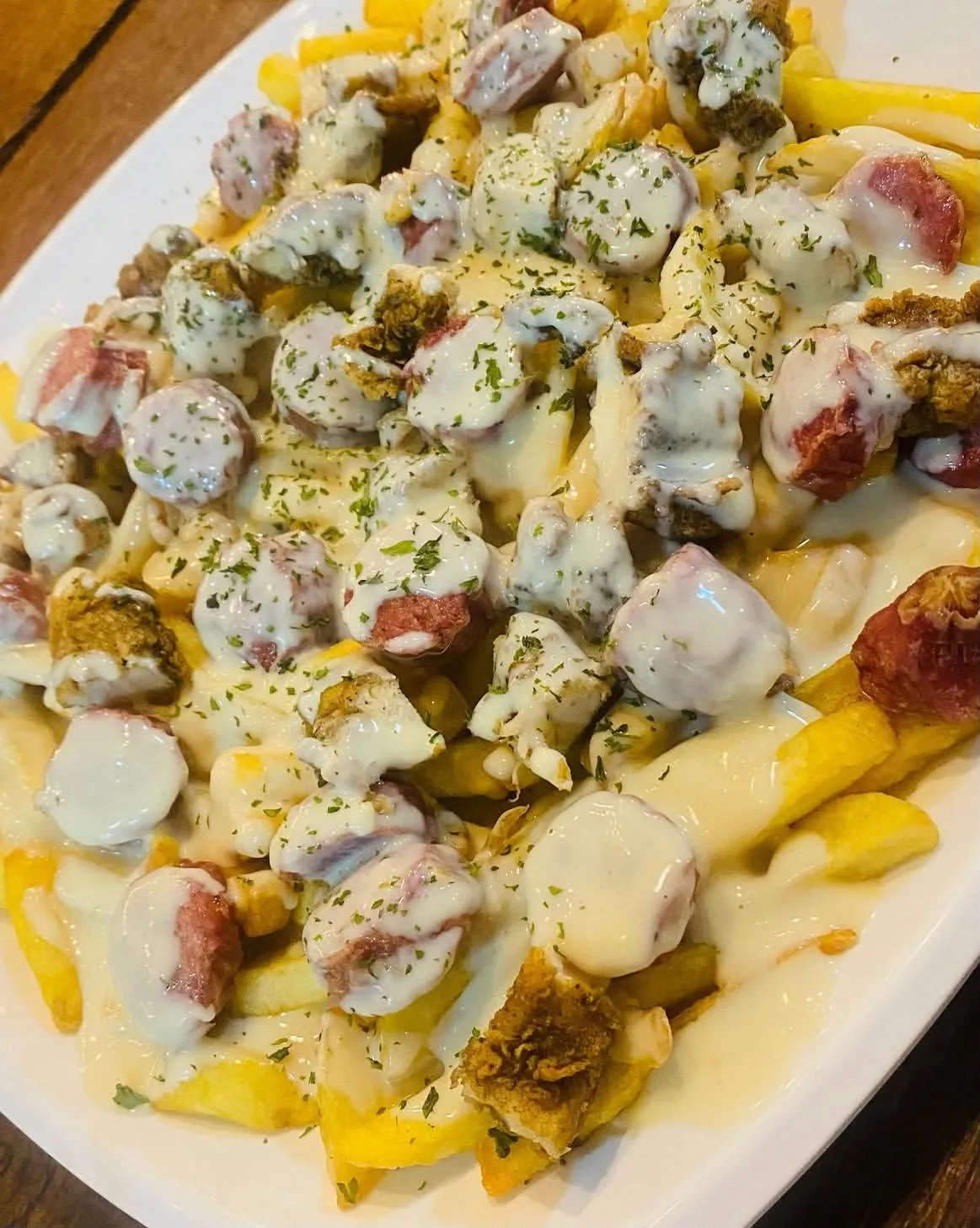 Plato de papas fritas con salchicha y abundante salsa de queso.