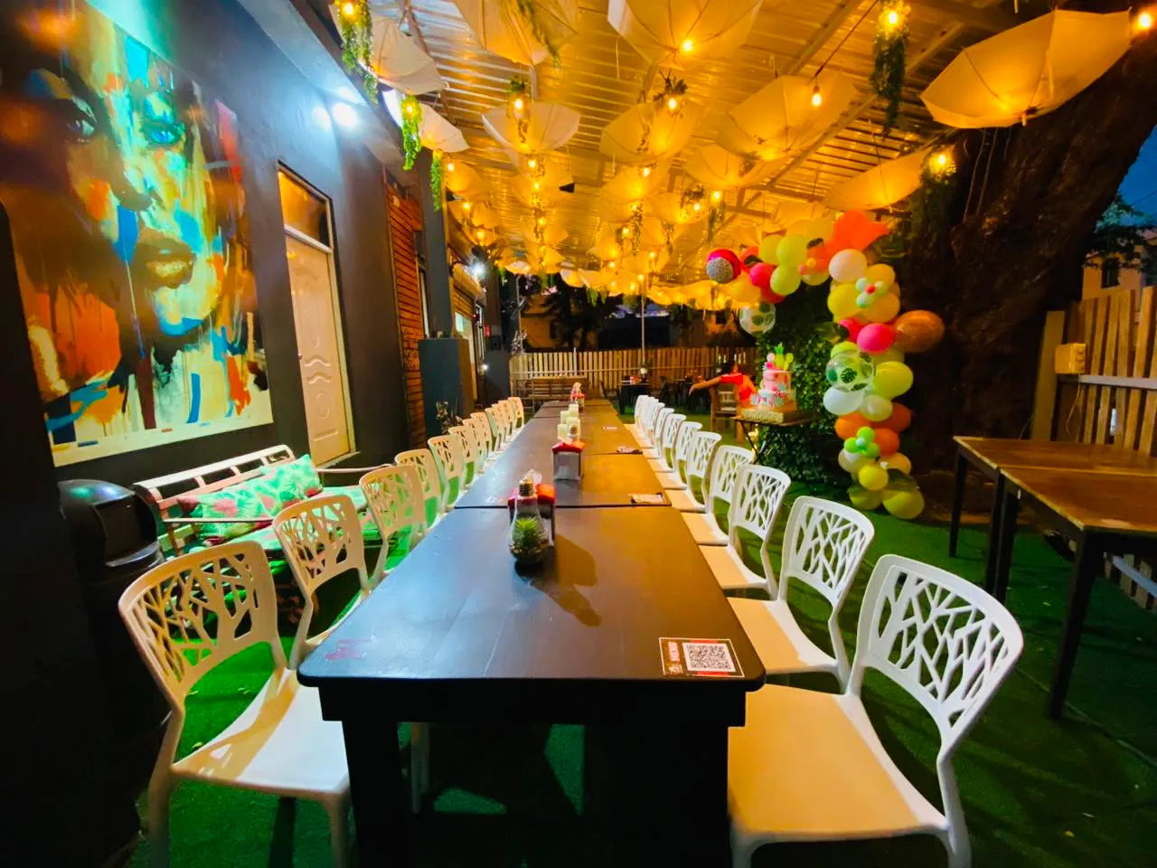 Mesa larga decorada para una celebración con globos y bizcocho.
